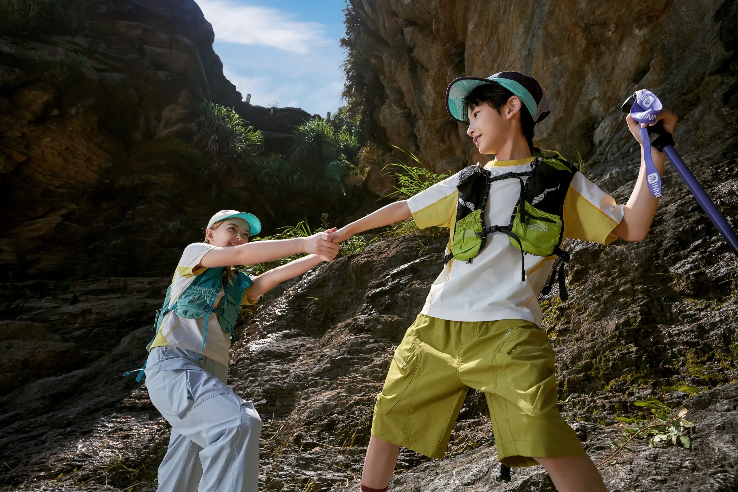 Two young explorers helping each other across a rocky trail