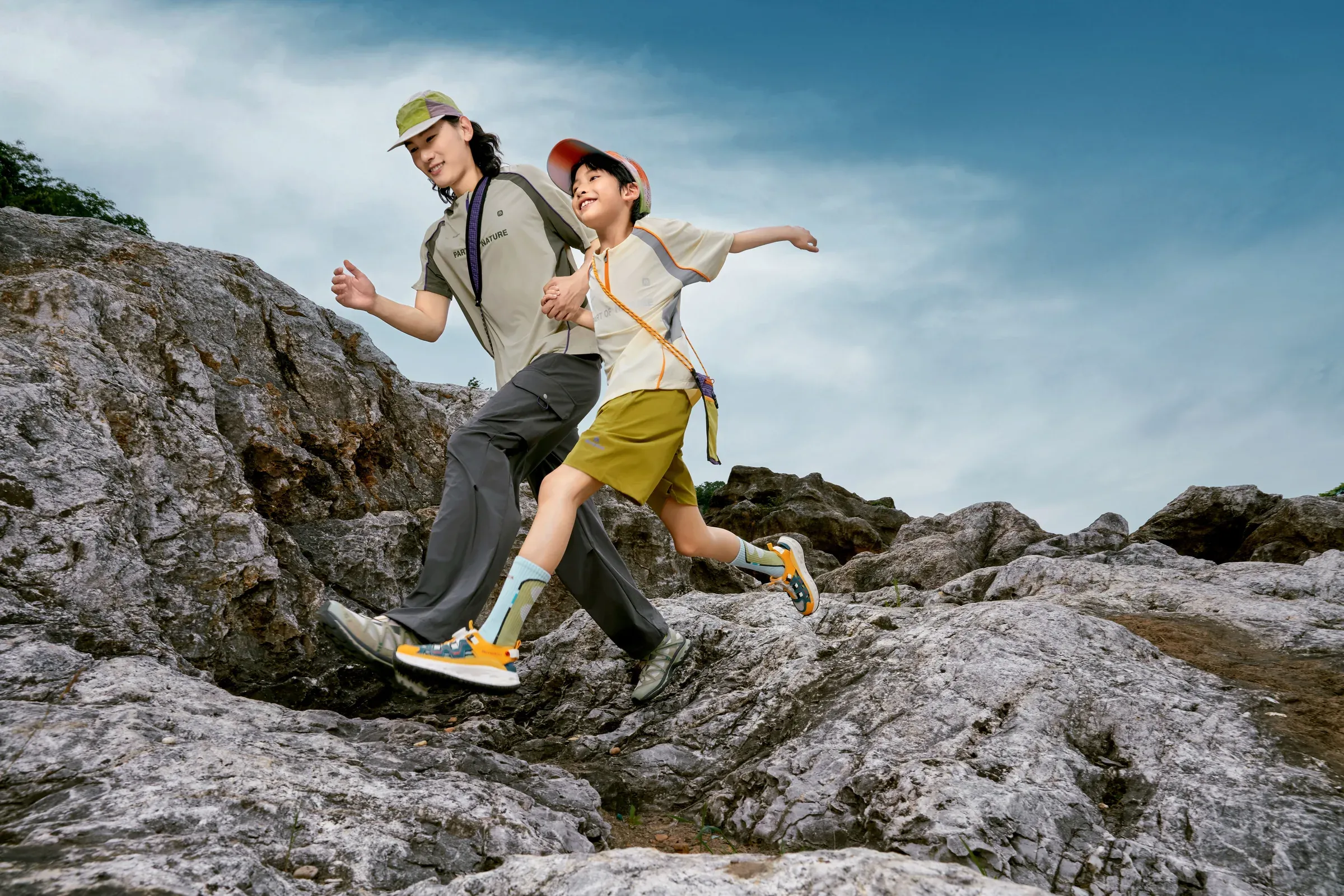 An adult and child running hand in hand over a rocky trail